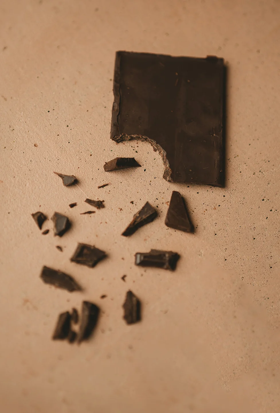 A broken bar of dark chocolate scattered across a warm stone surface